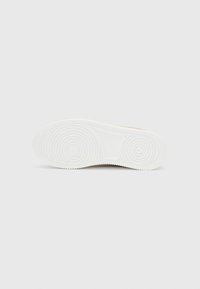 Semelle de chaussure en caoutchouc blanc présentant des motifs de bande de roulement circulaires, une texture lisse et une légère courbure améliorant le design pour le confort et l'adhérence.