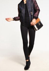 Svart bomberjacka med blommönster, svart åtsittande topp, svarta skinny jeans och svarta ankelskor. Axelväska med beige och svarta detaljer.