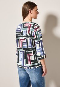 Camisa de manga larga con un colorido patrón geométrico con líneas rojas, azules, verdes y negras sobre un fondo claro. Corte holgado.