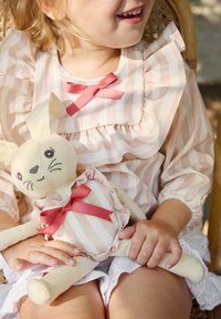 Randig, ljusrosa och vit blus med volangärmar, kompletterad av en mjuk kanindocka med fin textur och rosa banddetaljer.