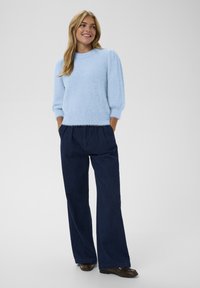 Jasnoniebieski, puszysty sweter z krótkimi, bufiastymi rękawami, w połączeniu z ciemnoniebieskimi spodniami o szerokiej nogawce i brązowymi butami. Gładka, miękka tekstura.