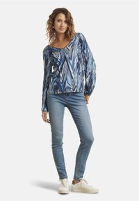 Blusa a maniche lunghe blu e bianca con motivo a zigzag, con scollo a V, abbinata a jeans blu chiaro e sneakers bianche. Tessuto dalla superficie liscia.