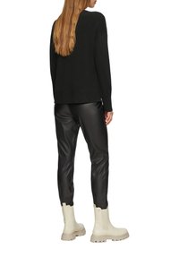 Zwarte gebreide trui, zwarte neplederen broek en crèmekleurige enkellaarzen met een gestructureerde afwerking en stevige zolen. Achteraanzicht, lang haar zichtbaar.