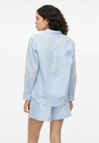 Light blue checkered shirt with long sleeves, buttoned cuffs, back pleat detail. Paired with matching shorts in a similar pattern.