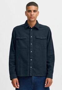 Dark blue, button-up shirt with two chest pockets, made of denim material. Features a classic collar and long sleeves with buttoned cuffs.