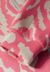 Bomullsmixat tyg med ett abstrakt mönster i rosa och krämfärg, med ribbat manschett och slät textur. Dragkedja synlig längs kanten.