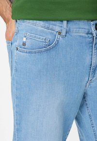 Jeans in denim azzurro chiaro con una texture liscia, dotati di una tasca frontale con un accento a motivo quadrettato e una chiusura a bottone in vita.