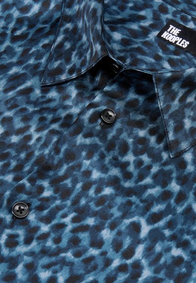 Shirt met een blauw-zwart luipaardprint, gemaakt van gladde stof. Voorzien van een puntenkraag en twee zwarte knopen op de sluiting.