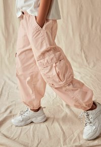 Roze cargobroek met zijzakken, elastische boorden en een gerimpelde tailleband. Gepaarde met witte sneakers met textuurdetails en veters.