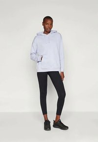 Helle blaue Kapuzenjacke mit einer Taschenfront und verstellbarem Kordelzug, kombiniert mit schwarzen Leggings und schwarzen Turnschuhen. Glatte Textur, lässiges Design.