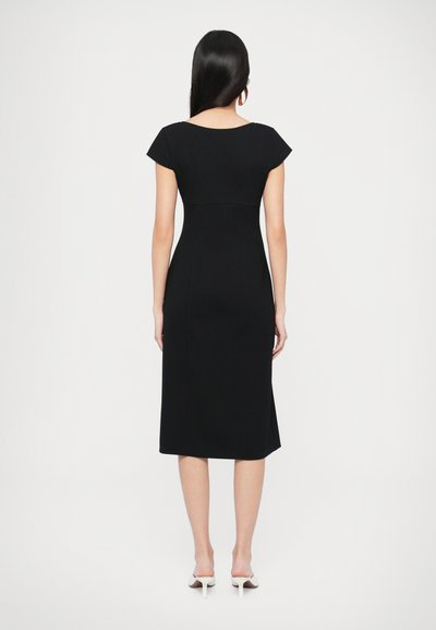 Melna midi kleita ar kapu piedurknēm un pieguļošu bodiju, gludu tekstūru un izplestu svārku. Valkāta kopā ar baltām atvērtām augstpapēžu kurpēm.