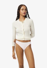 Crèmekleurige geribbelde cardigan met een ronde halslijn en knoopsluiting, gecombineerd met lichtroze ondergoed met een merkband.