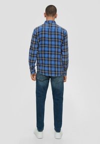 Blauw en zwart geruit overhemd met lange mouwen, button-down kraag en gebogen zoom, gecombineerd met donkerblauwe jeans en witte sneakers.