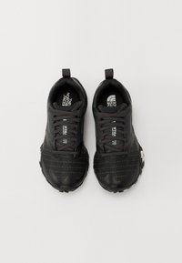 Chaussures de sport noires avec une tige synthétique texturée, motif rayé ton sur ton, semelle en caoutchouc et accents de marque sur les côtés et la languette.