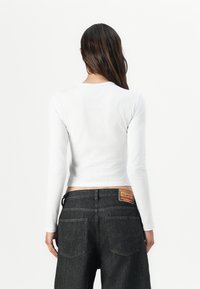 Haut à manches longues blanc avec un col rond, associé à un jean en denim foncé doté de poches arrière et d'une étiquette sur la taille.