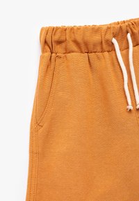Chinoises en coton orange avec une taille élastique à cordon de serrage, une poche latérale et une texture lisse.