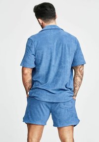 Completo in felpa blu, composto da una maglietta a maniche corte e pantaloni corti, con colletto classico, texture morbida e vestibilità comoda.