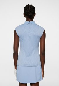 Vaaleansininen hihaton polo paita, jossa on teksturoitu kuvio, kaulus ja pieni takalukko; yhdistettynä samaa sävyä olevaan kevyeen hameeseen.