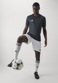 Sort Adidas trøje, hvide shorts med tre striber, hvide sokker med sorte detaljer, sorte fodboldsko, jonglerer med en sort og hvid fodbold.