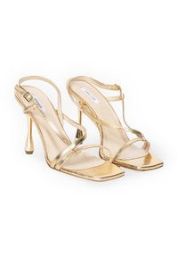 Złote metaliczne sandały na wysokim obcasie z otwartym palcem, kwadratowym kształcie i wieloma cienkimi paskami. Posiadają elegancki, zaokrąglony obcas i regulowane zapięcie.