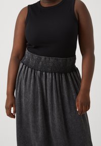 Svart ribbad linne kombinerat med en grå smockad midja kjol med samlad tyg, vilket ger en svävande silhuett.