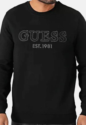 Chemise noire à manches longues avec le mot "GUESS" en motif pointillé et "EST. 1981" imprimé en dessous sur la poitrine.