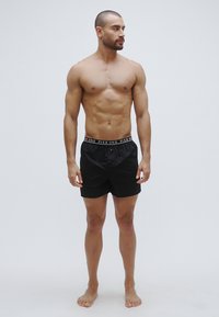 Boxer noirs avec une ceinture arborant le texte "PIER ONE" en blanc. Design simple, tissu léger et coupe ample.