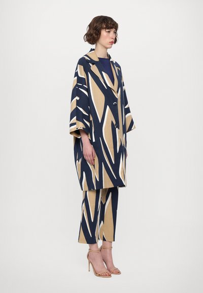 Navy and beige patterned oversized coat with wide sleeves, featuring large abstract shapes and front buttons, paired with matching cropped pants.