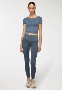 Completo sportivo blu composto da una maglietta aderente a maniche corte e leggings a vita alta, entrambi realizzati in un materiale liscio e elastico.