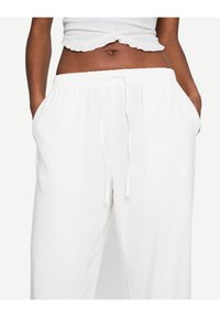 Bílé lněné kalhoty s elastickým pasem, stahovací šňůrkou a bočními kapsami. Měkká textura a uvolněný střih, ideální pro každodenní nošení.