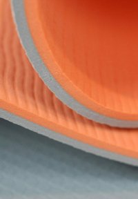 Flexibla orange gummiplattor med en strukturerad yta, lager på lager över en slät grå bas, som visar upp rundade kanter och kontrasterande färger.