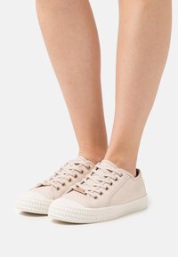 Lys rosa lerretssneakers med hvite gummisåler, med gulløyler og sn�ørebånd, rund tå og teksturert mønster på sålen.