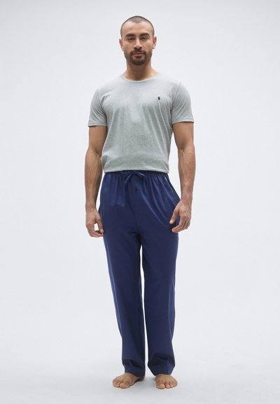 Szara bawełniana koszulka z okrągłym dekoltem, zestawiona z niebieskimi spodniami z sznurkiem. Spodnie mają luźny krój i fakturowaną tkaninę.