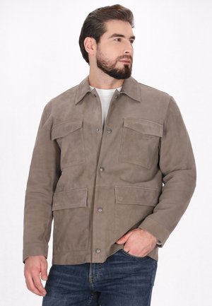 Jachetă din suede maro deschis, cu închidere cu bătaie, două buzunare pe piept și două buzunare laterale. Prezintă un guler clasic și o textură netedă.