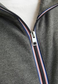 Sivá bundová mikina na zips s čiernym zipsom a pruhovanými akcentami v červenej, bielej a modrej farbe pozdĺž goliera, vyrobená z mäkkej, štruktúrovanej tkaniny.