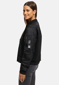 Black bomber jacket with a sleek, smooth texture. Includes zippered pockets and a ribbed collar. Features detailing on the sleeve.