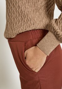 Bruine gebreide trui met een gestructureerd golfpatroon, gecombineerd met roestbruine broeken met zijzakken en een losse pasvorm.