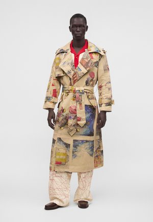 Hombre con gabardina beige con estampados vintage coloridos de viajes y globos aerostáticos sobre pantalones crema de pierna ancha con líneas abstractas rojas.