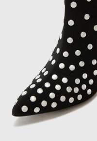 Black ankle boot with a pointed toe, covered in silver studs. Made of a stretchy fabric, featuring a close-fitting design.