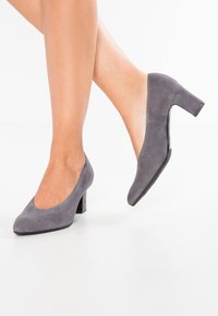 Chaussures à talons hauts en suede gris avec un bout rond et un talon carré. La texture est douce, avec une finition lisse et peu de détails.