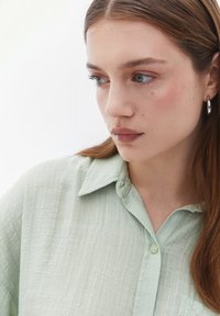 Lichtgroene, gestructureerde button-up shirt met een kraag. Heeft een subtiel kreukpatroon en een zak. Het haar van het model is los.