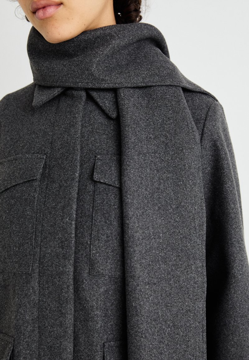 Grau Wollmantel mit breitem Schalkragen, ausgestattet mit zwei Vordertaschen und einer weichen, strukturierten Oberflächenbeschaffenheit, entworfen für Wärme und Komfort.