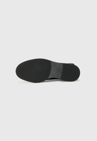 Suela de zapato negra, de forma redondeada, textura de goma lisa, con marca en relieve y detalles mínimos, que proporciona una apariencia elegante.