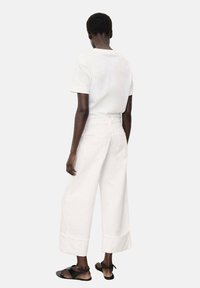 White cotton t-shirt with short sleeves and relaxed fit, paired with white wide-leg denim pants featuring large pockets and a straight hem.