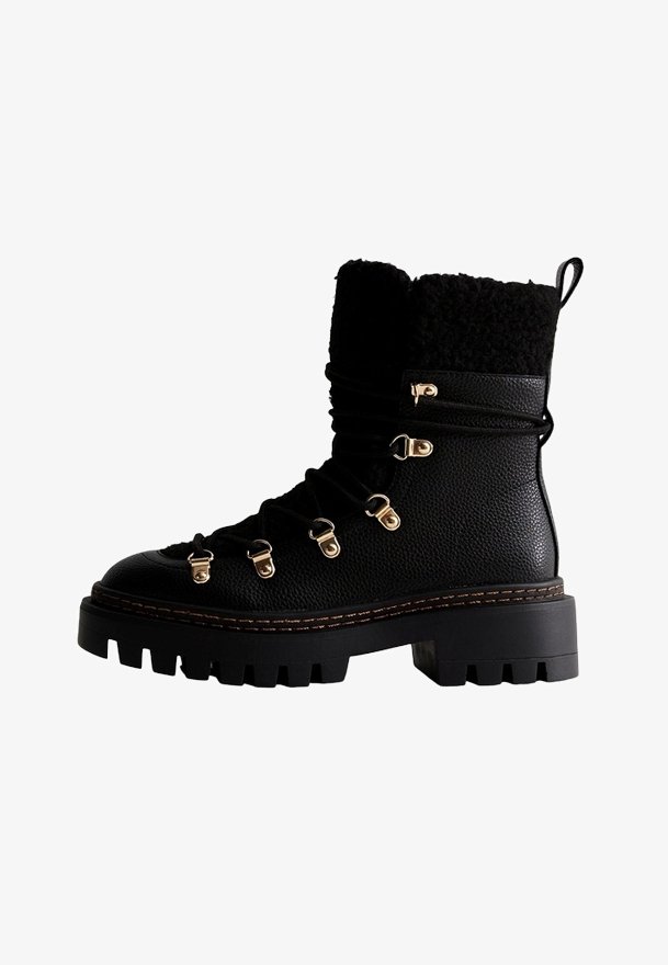 Botte noire à lacets jusqu'à la cheville en cuir texturé, col en fausse fourrure, œillets dorés, et semelle en caoutchouc robuste et épaisse. Détails avec des accents de couture.