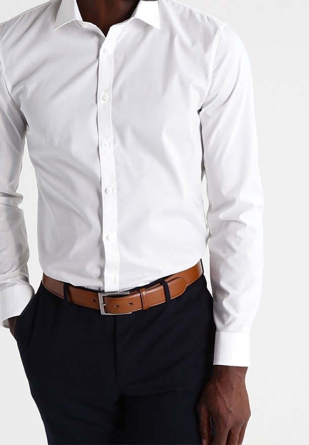 Vit bomullsskjorta med slät textur, utrustad med klassisk krage och dold knappslå, kombinerad med ett brunt läderbälte.