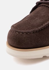 Καφετί σουέντ παπούτσι με στρογγυλεμένη μύτη, ορατή ραφή και υφή στην κρεμ σόλα. Λείο επάνω μέρος χωρίς ορατά λογότυπα.