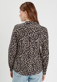 Blouse noire à manches longues avec un motif léopard en beige et blanc. Dotée d'un col classique et de détails de poignet boutonnés.