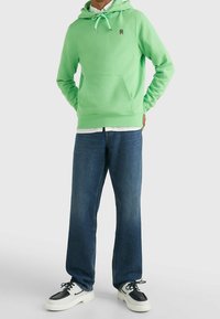 Felpa verde menta con tasca a marsupio, cordino regolabile e piccolo logo. Abbinata a jeans in denim blu larghi e sneakers bianche.