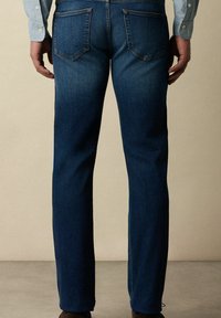 Tmavě modré džíny s rovnými nohavicemi, viditelným šitím a dvěma zadními kapsami. Hladká textura s mírným vyblednutím v okolí švů.